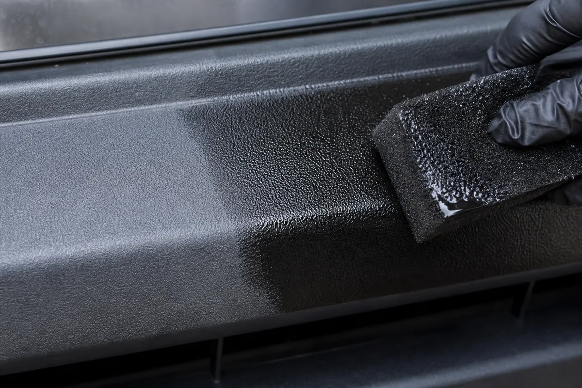 Application d’un rénovateur de plastique noir sur un pare-choc avec un applicateur en mousse